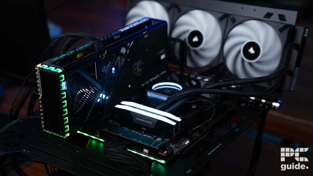 An illuminated gaming computer motherboard with Ryzen 7 7700X, graphics card, and cooling fans, showcased in a dimly lit environment.